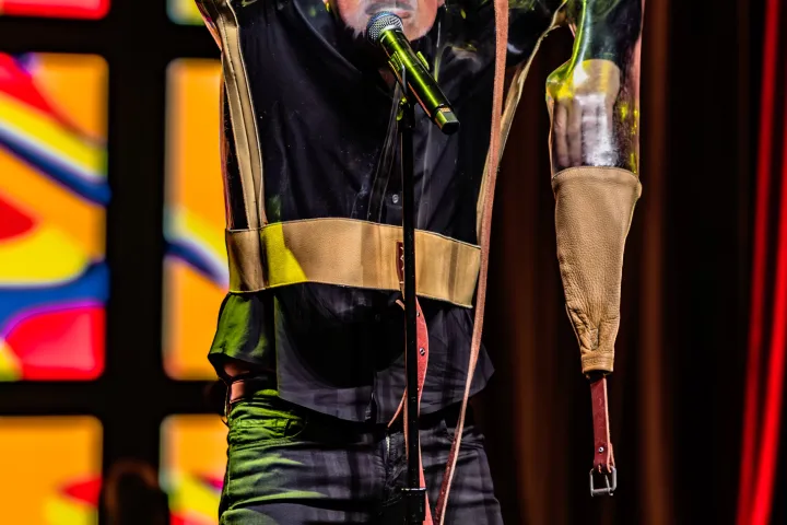 Person on stage in straitjacket with microphone, colorful background.