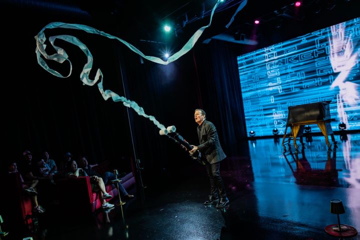 Performer on stage shooting streamers from a device, with an audience watching.