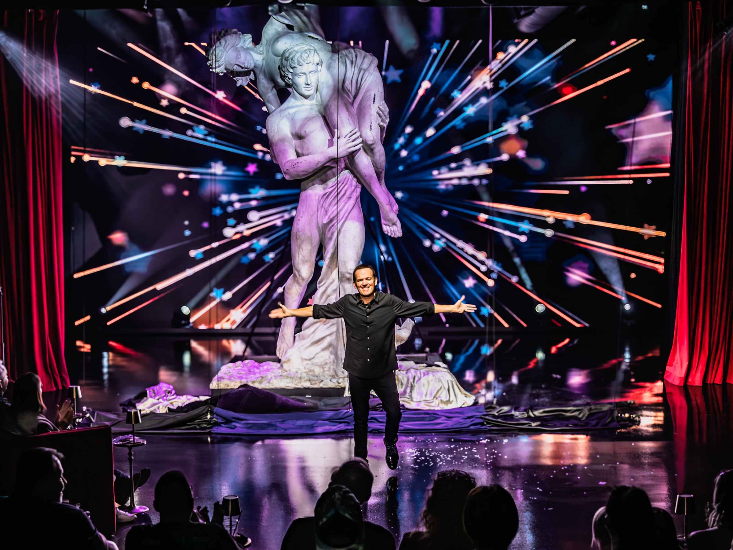 Performer on stage with large statue in background and audience clapping.